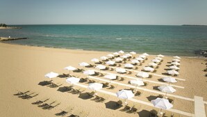 Ein Strand mit Reihen von Liegestühlen und weißen Sonnenschirmen, einem klaren Himmel und ruhigem Meer.