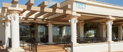 A building with a covered outdoor seating area, columns, and a staircase leading to the entrance.