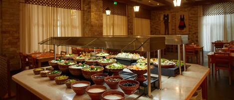 A buffet area with various food dishes displayed in bowls and platters, with a counter and seating area in the background.
