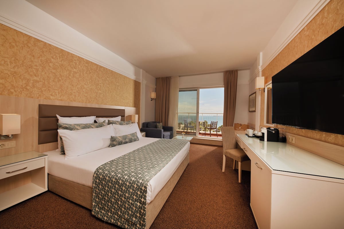 Een hotelkamer met een groot bed, een bureau, een stoel, een televisie en een balkon met uitzicht.
