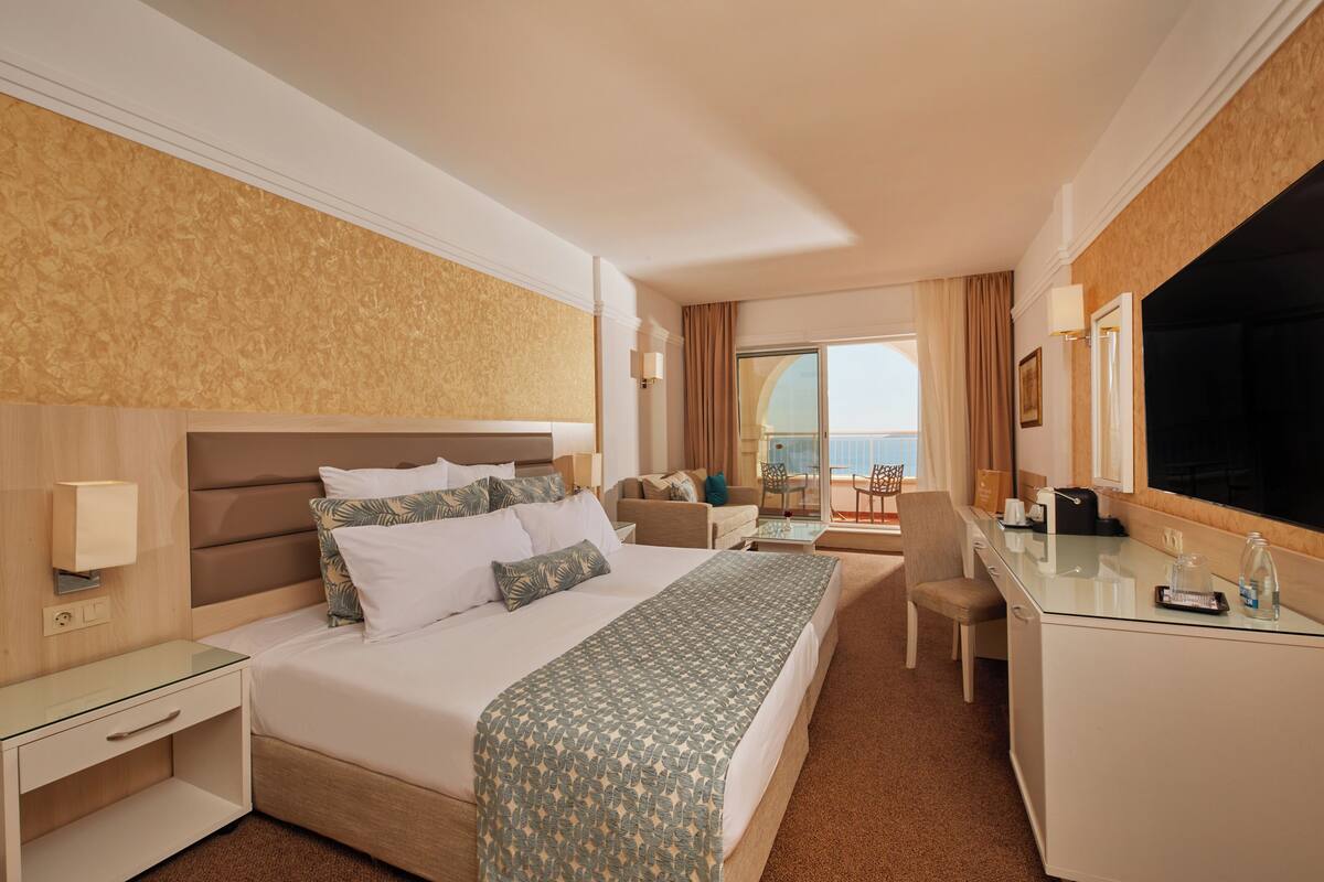 Een hotelkamer met een groot bed, een bureau, een stoel en een balkon met uitzicht.