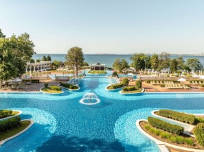 A large swimming pool with a central water feature, surrounded by lounge areas and trees.
