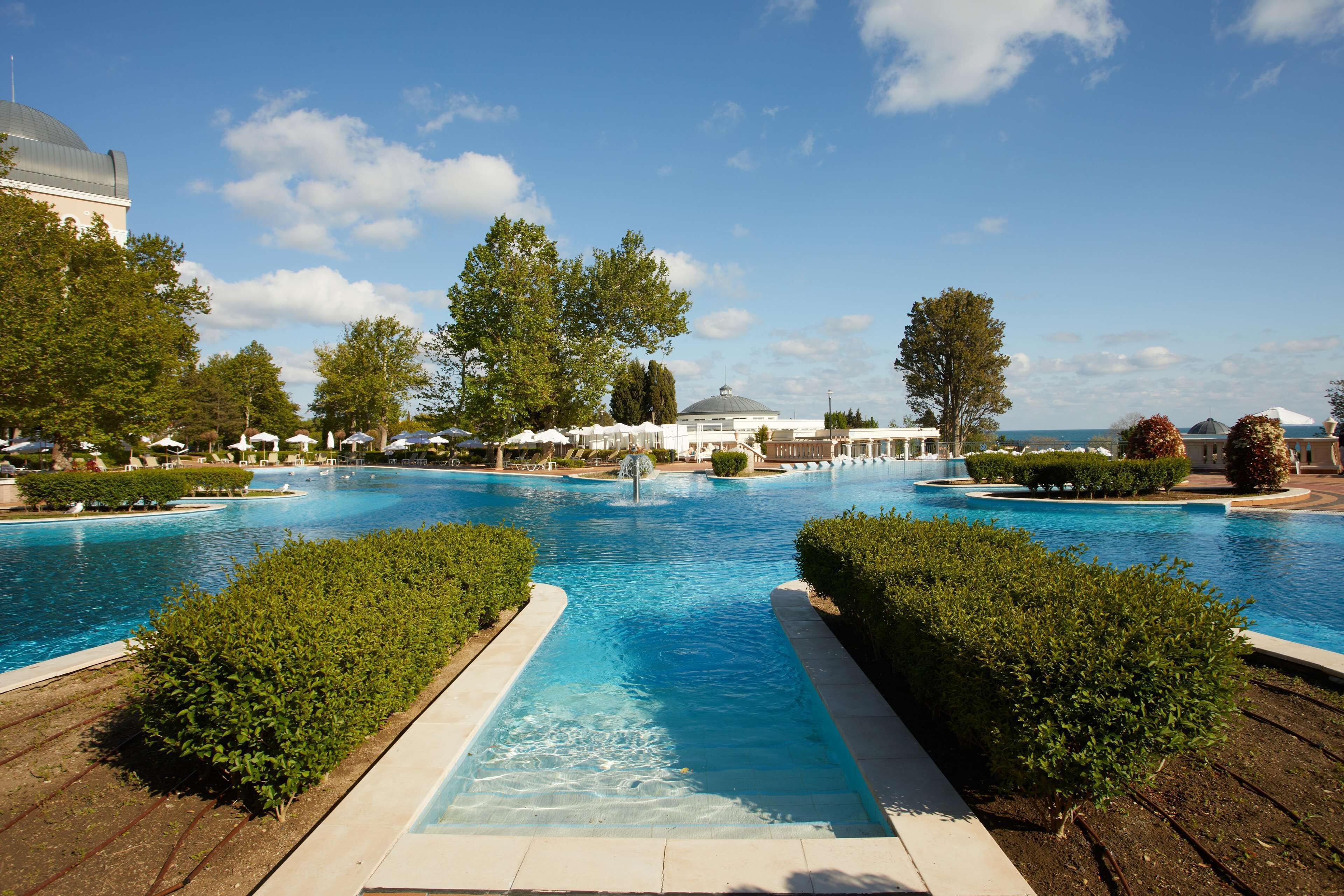 A large outdoor swimming pool with a clear blue sky and a building with a dome in the background.
