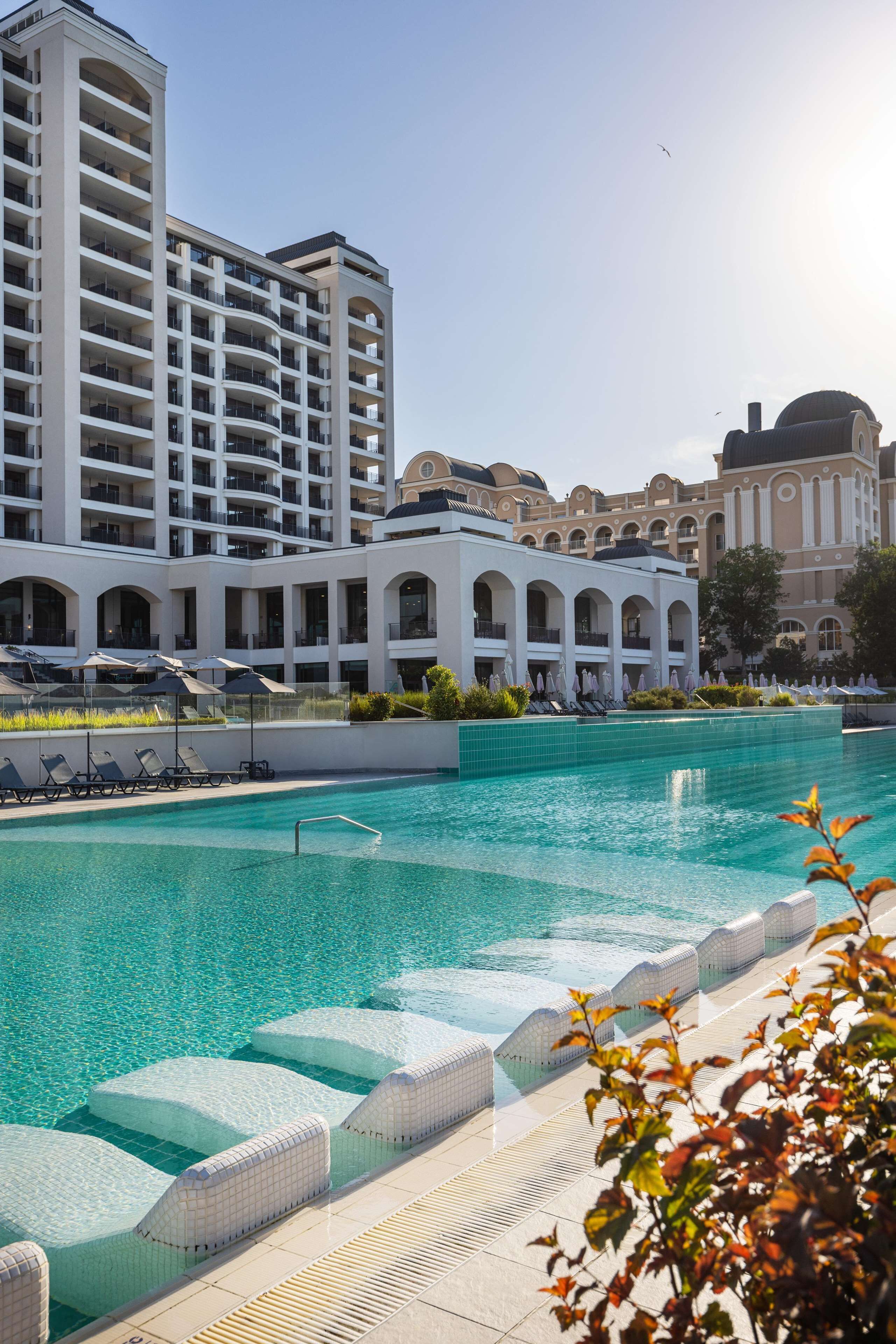 A hotel with a large pool, multiple balconies, and a classical architectural style.