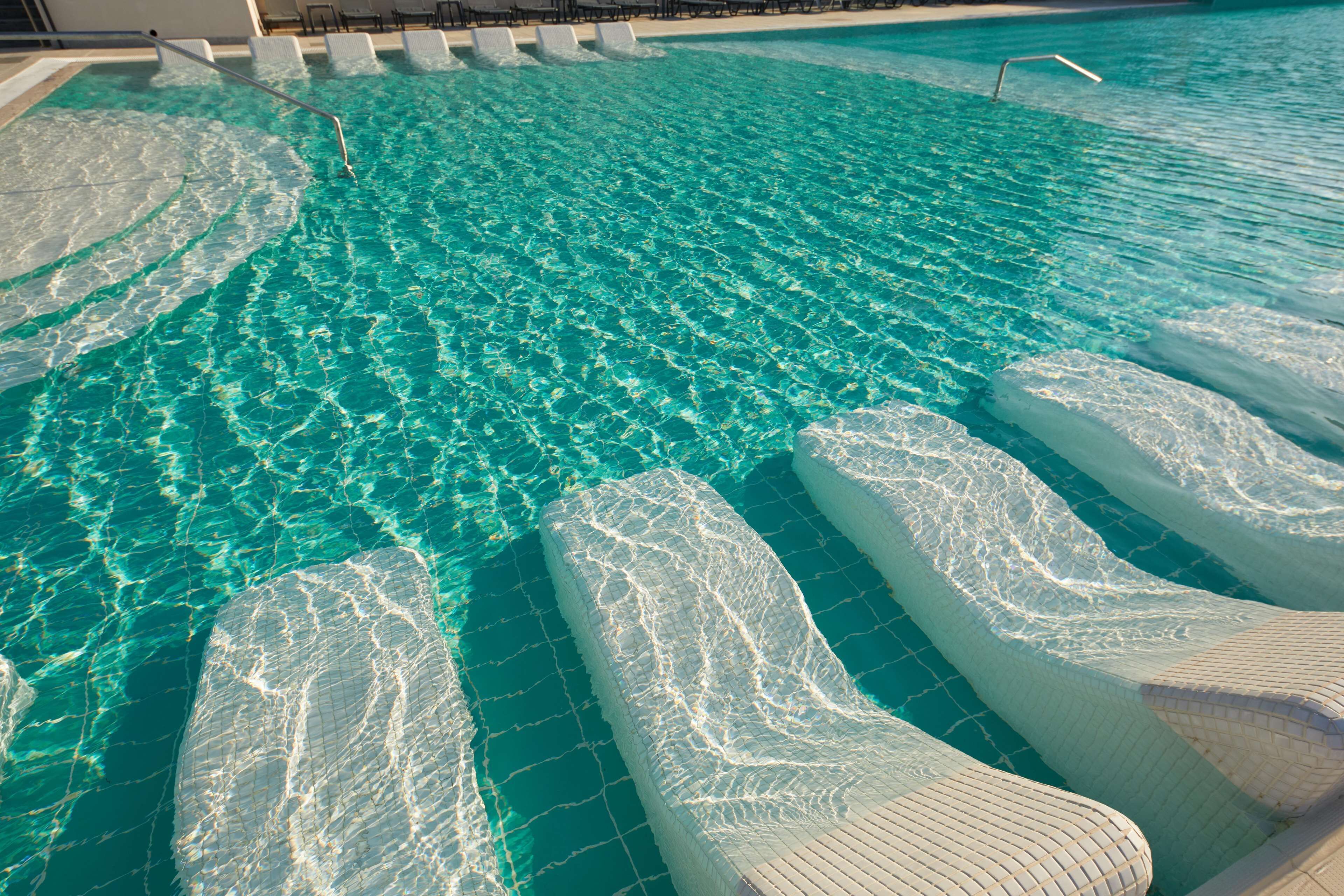 Piscina limpia con escalones para entrar al agua, rodeada de sillas de descanso.