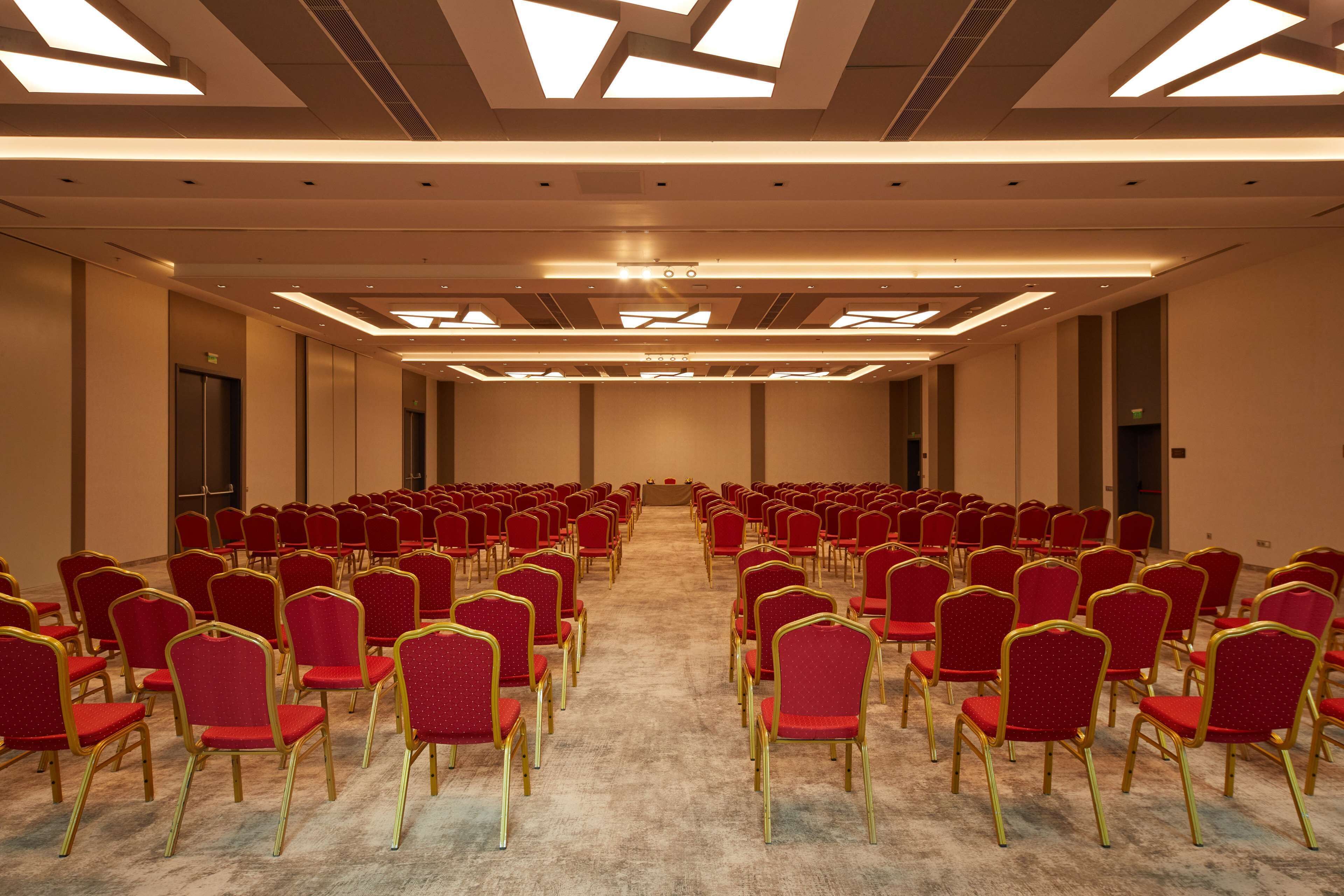 A conference room with rows of red chairs and a podium at the front.