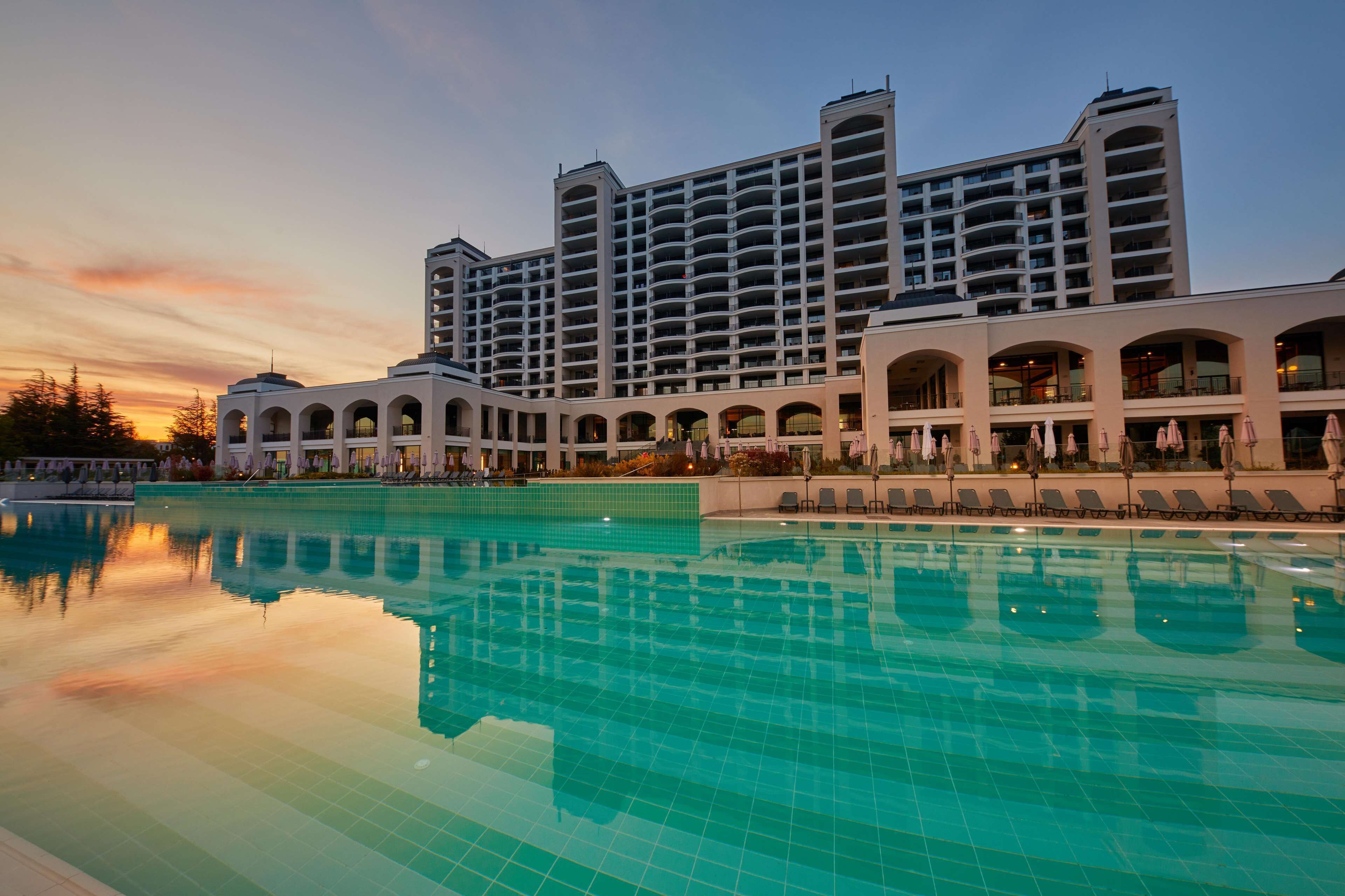 A hotel with a large pool, multiple balconies, and a modern architectural design.