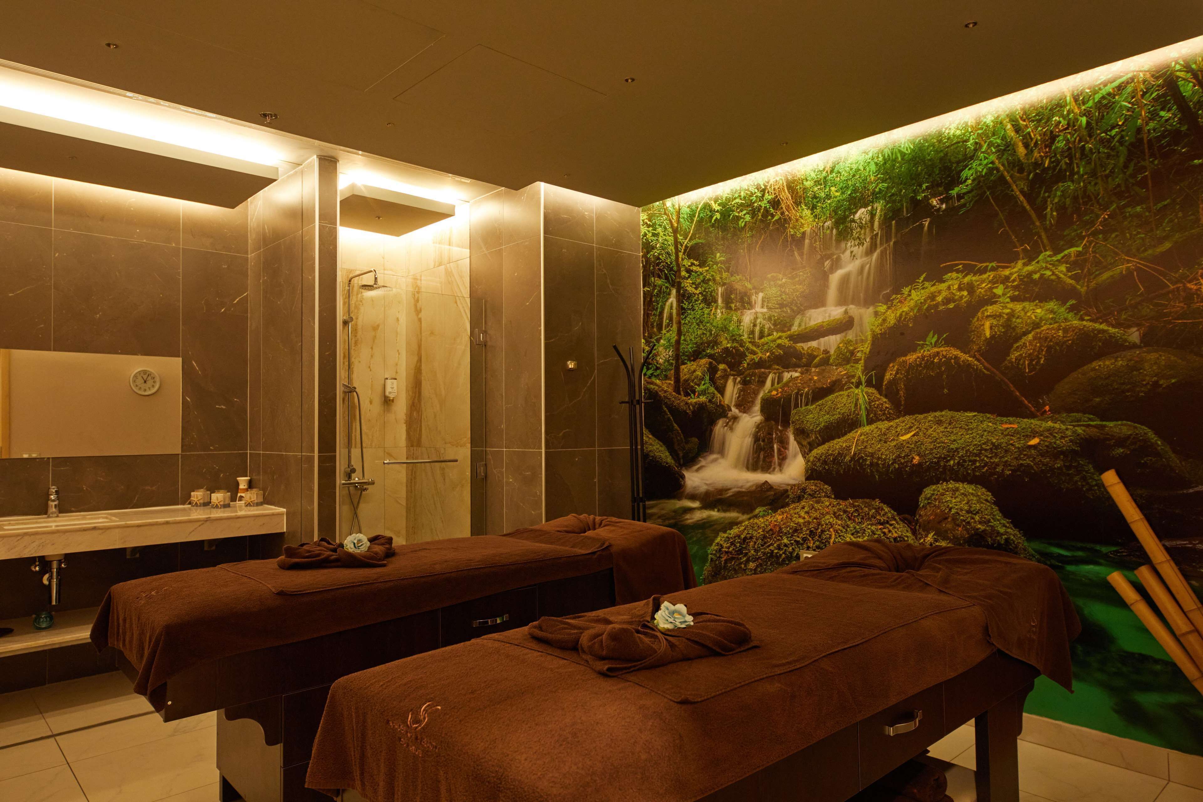 A spa room with two massage tables, a sink, and a wall mural of a waterfall.