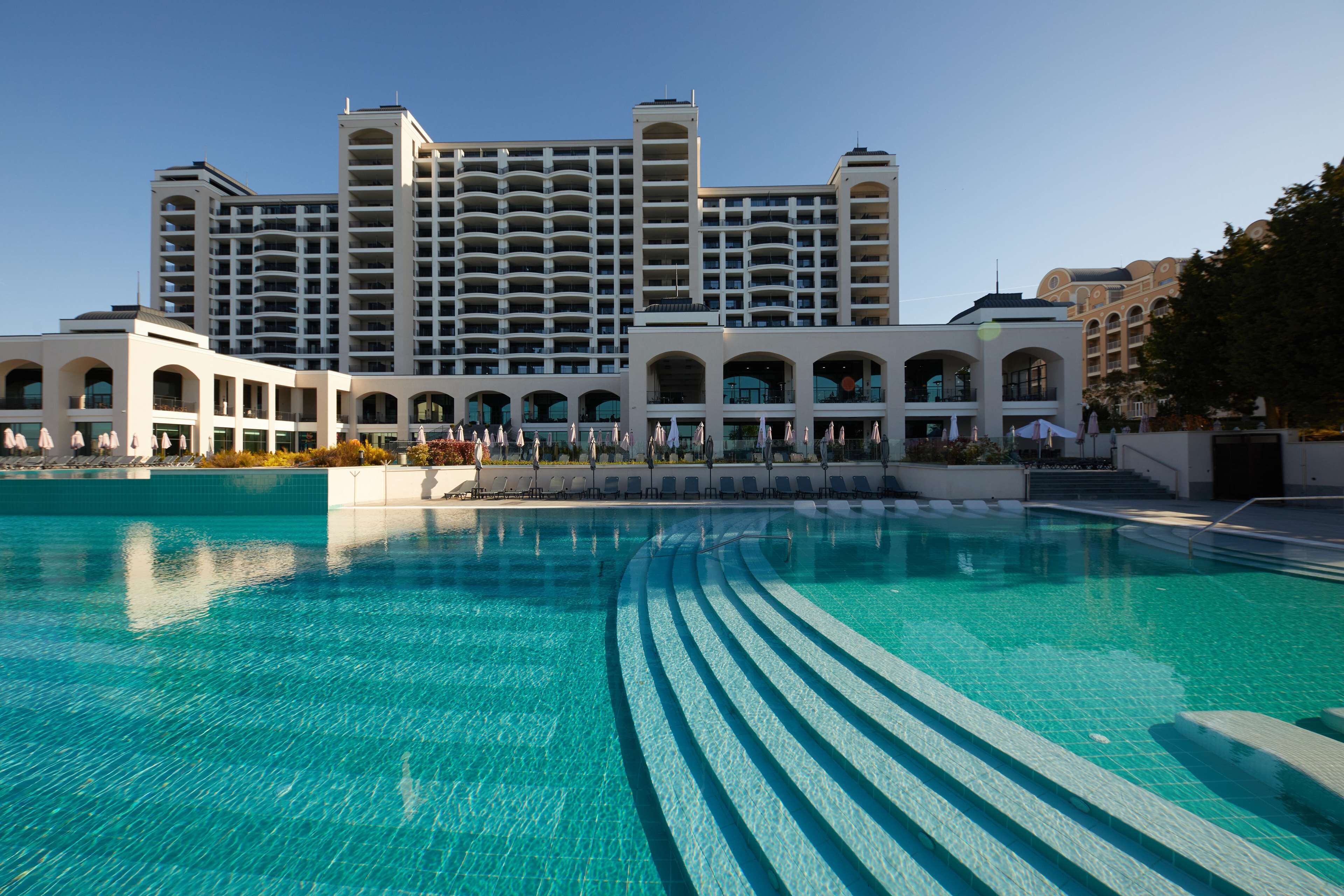 A hotel with a large swimming pool, multiple balconies, and a modern architectural design.