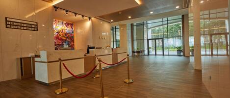 A reception area with a marble reception desk, a red rope barrier, and a large abstract painting on the wall.