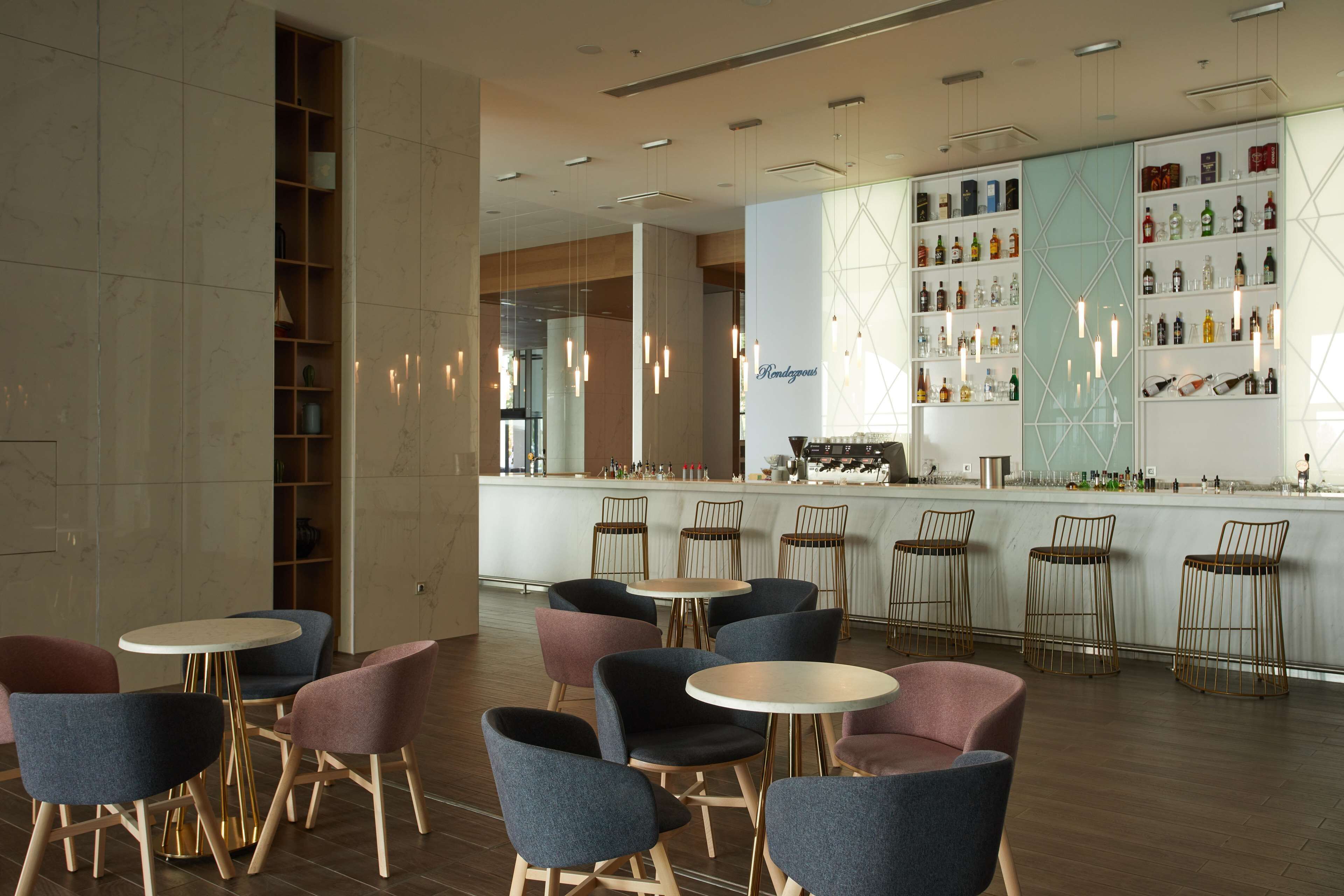 A modern bar area with round tables and chairs, a well-stocked liquor shelf, and a visible kitchen in the background.