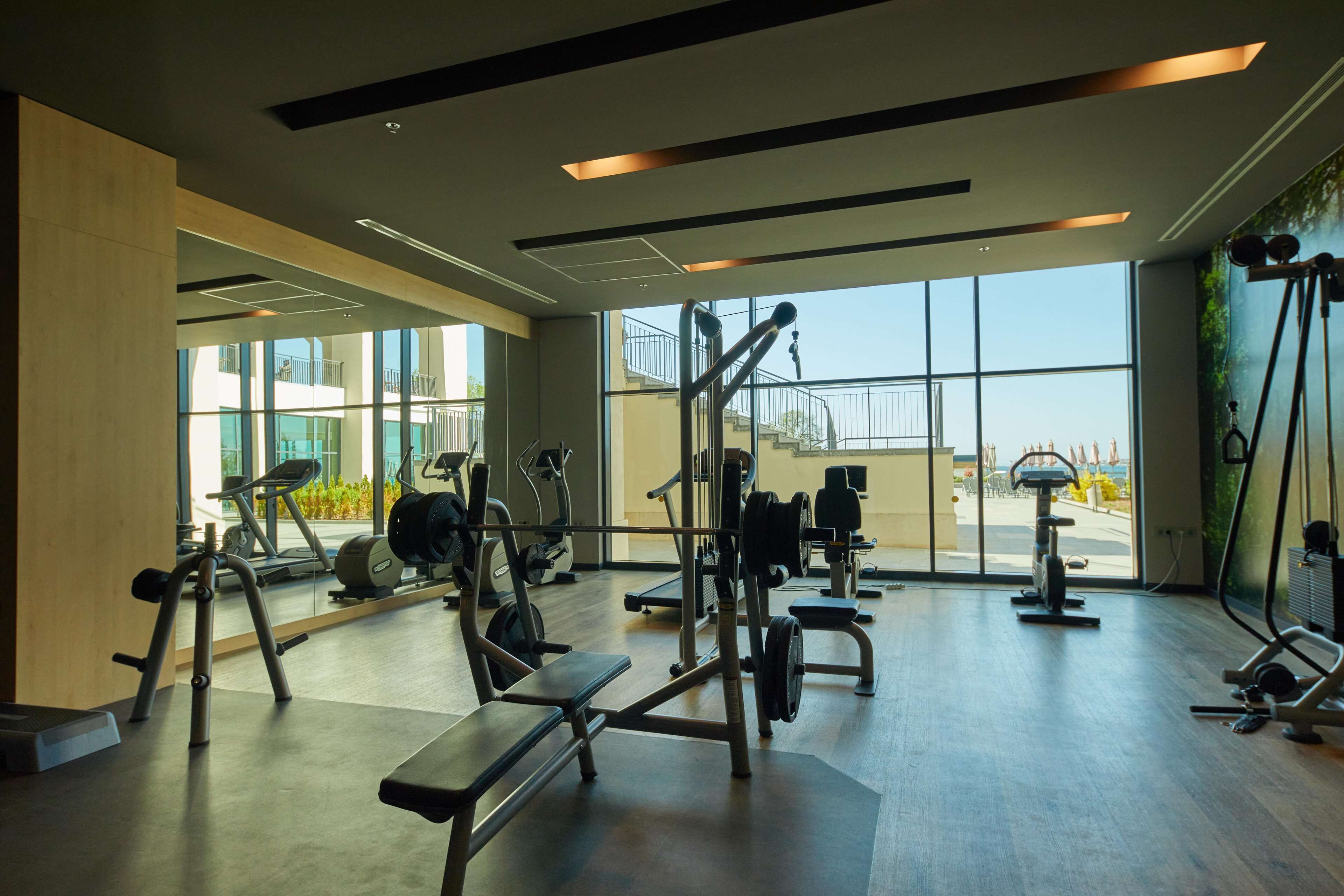 Un gimnasio moderno con diversos equipos de ejercicio, ventanas amplias y vistas al exterior.