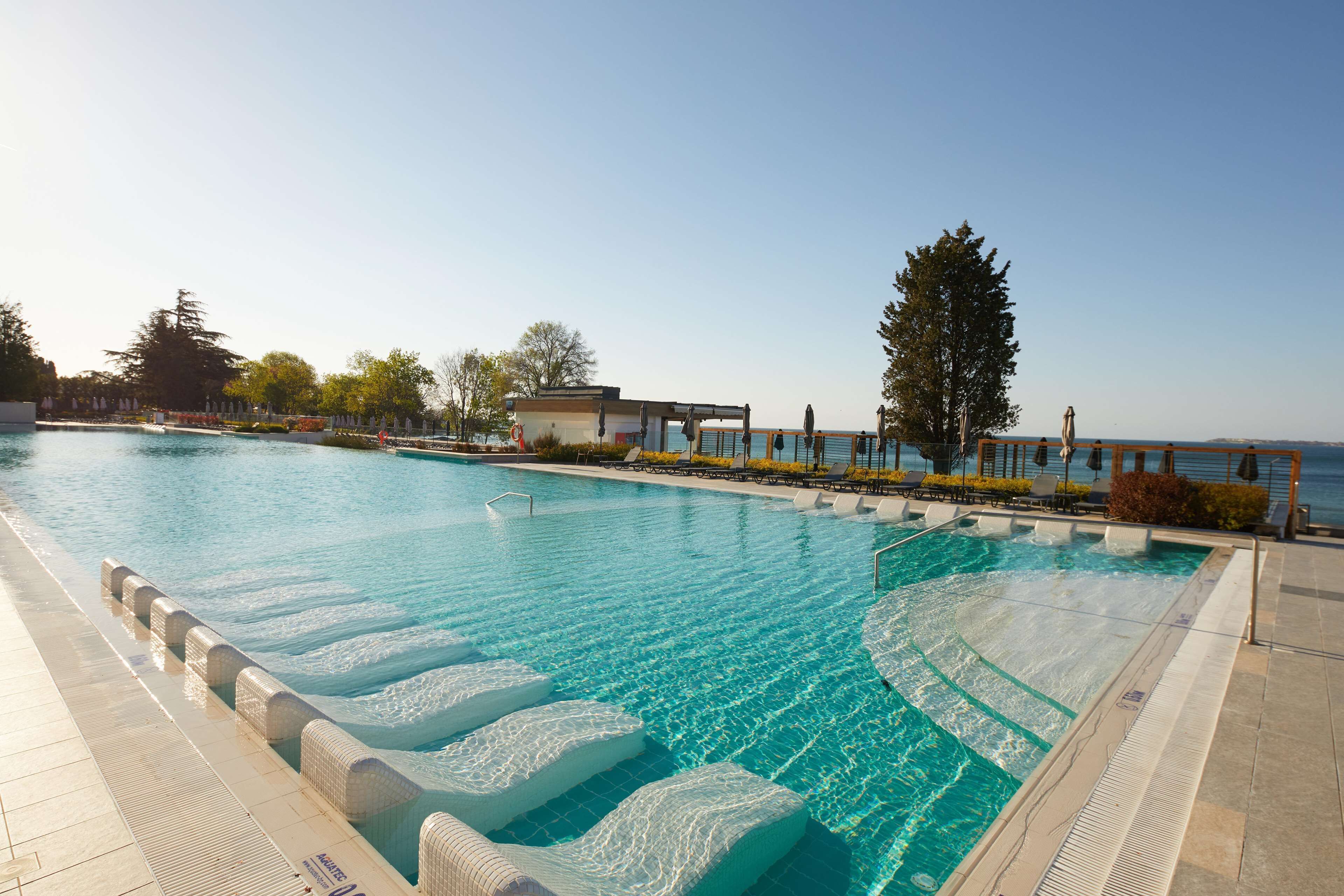A swimming pool with clear blue water, surrounded by lounge chairs and a view of the sea.