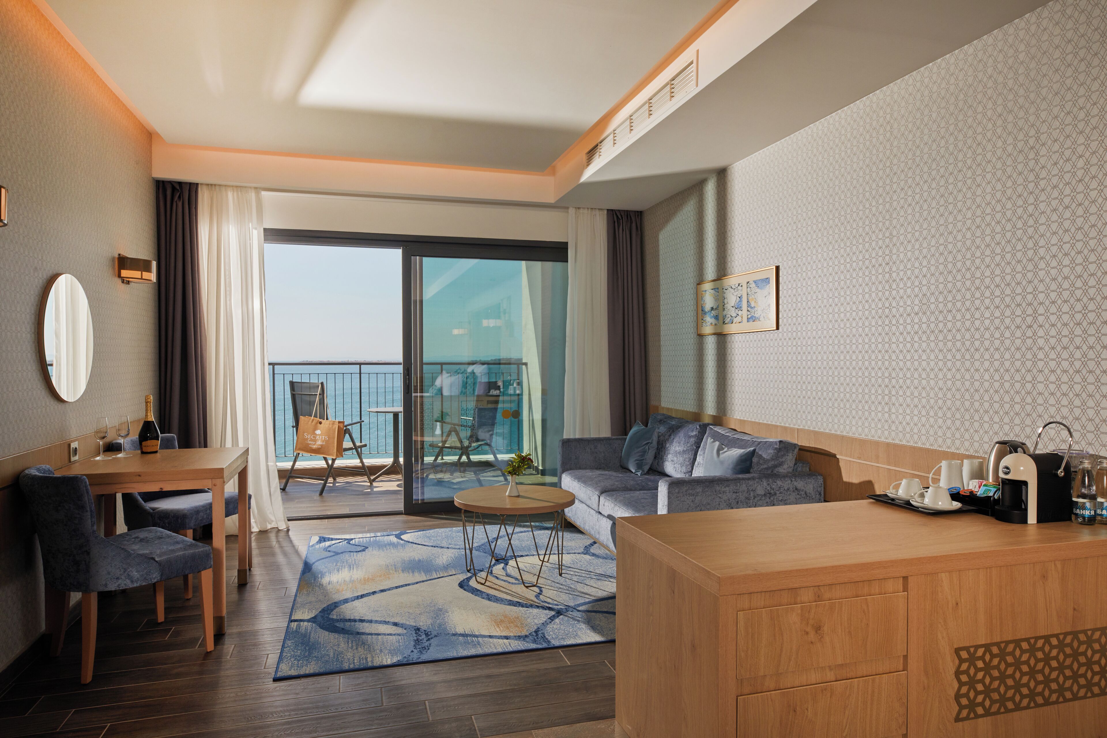 Habitación de hotel moderna con balcón, zona de comedor, sofá y mostrador de cocina.