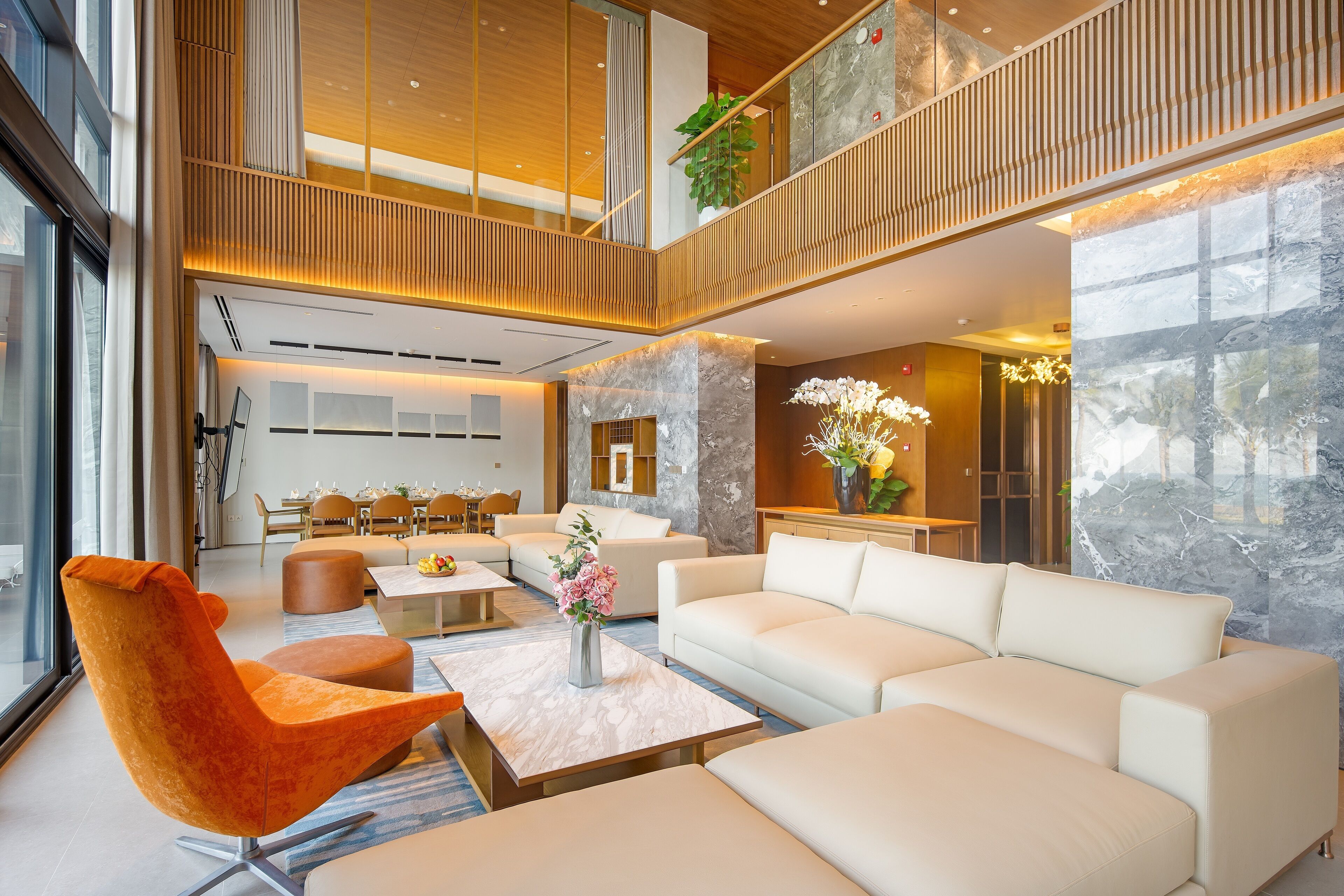 A modern hotel lobby with a high ceiling, a dining area, and a seating area with a sofa and chairs.