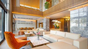 A modern hotel lobby with a high ceiling, a dining area, and a seating area with a sofa and chairs.
