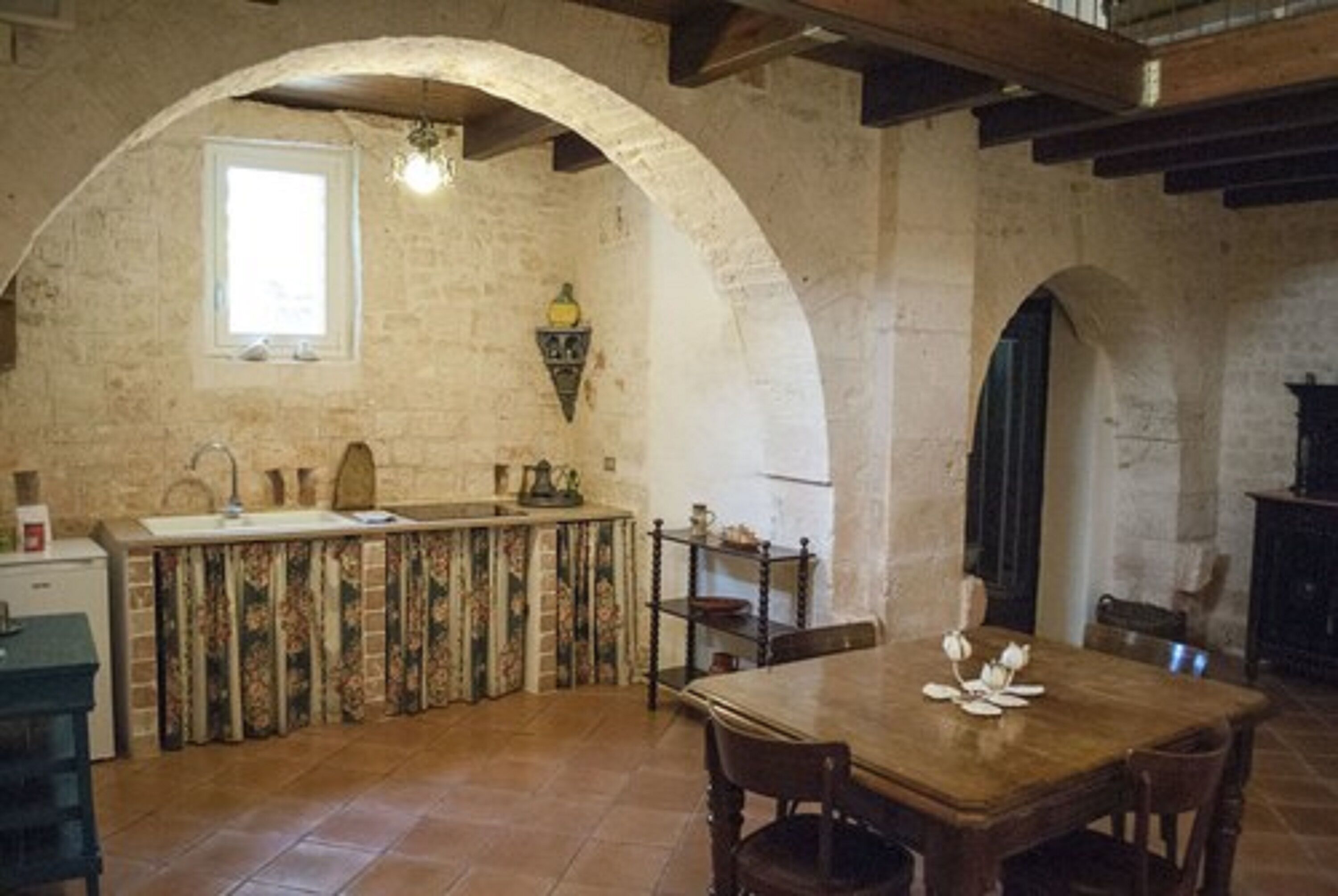 A rustic kitchen with a stone arch, a wooden table, and a window.