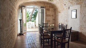 A stone-walled dining area with a table and chairs, a window with curtains, and a view of the outdoors. - Agriturismo Antonelli Piangevino (Monopoli)