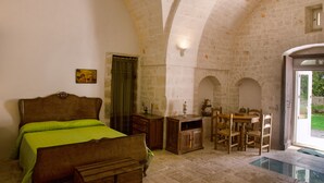A bedroom with a bed, a wooden dresser, a table with chairs, and a glass-enclosed area. - Agriturismo Antonelli Piangevino (Monopoli)