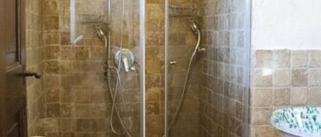 A glass-enclosed shower with a stone-tiled wall, a wooden door, and a white basin on a wooden stool.