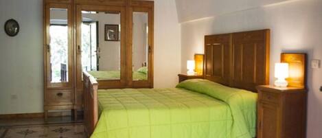Un dormitorio con cama, armario de madera, lámparas de noche y un espejo.