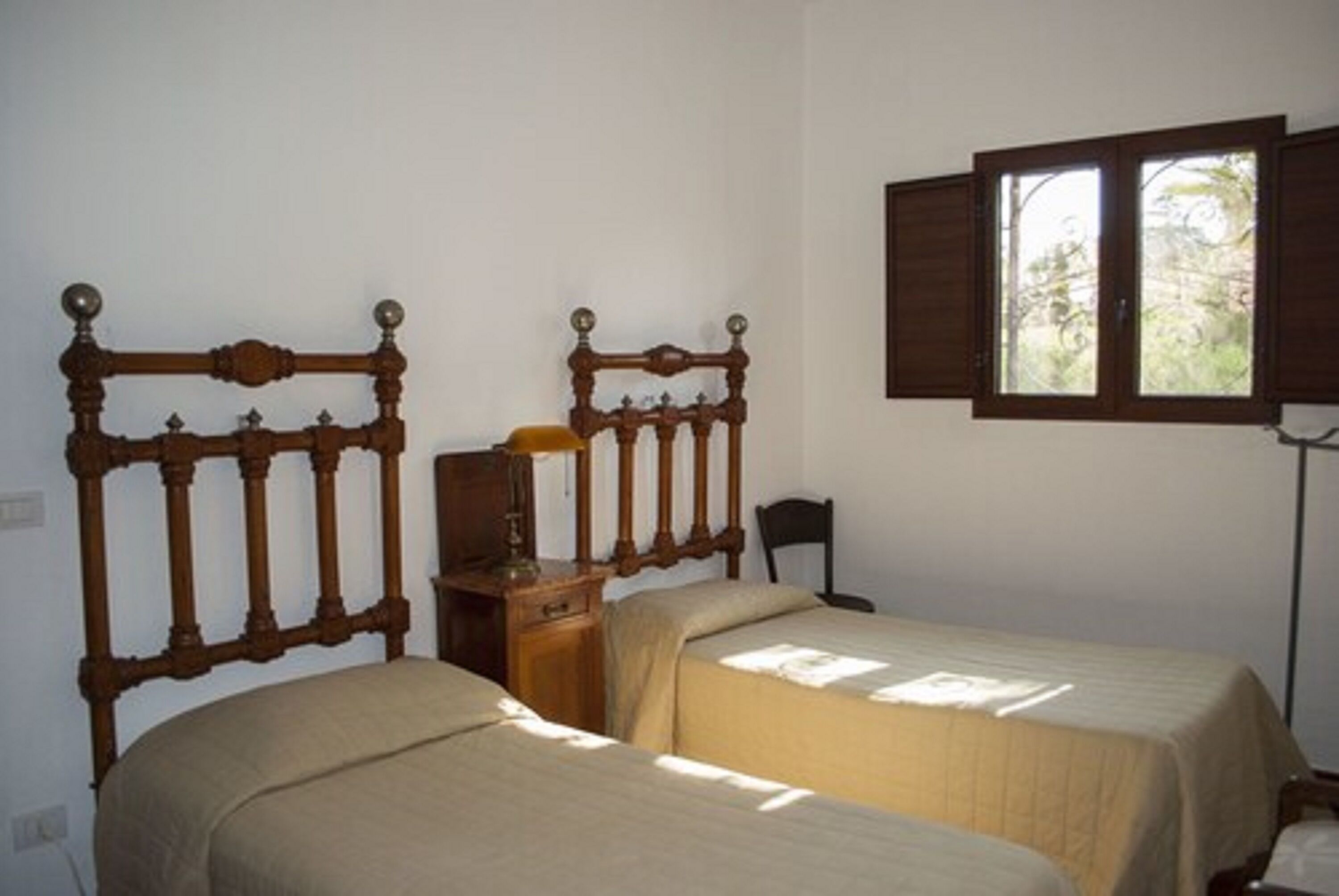 A room with two wooden beds with headboards, a nightstand, a lamp, and a window with shutters.