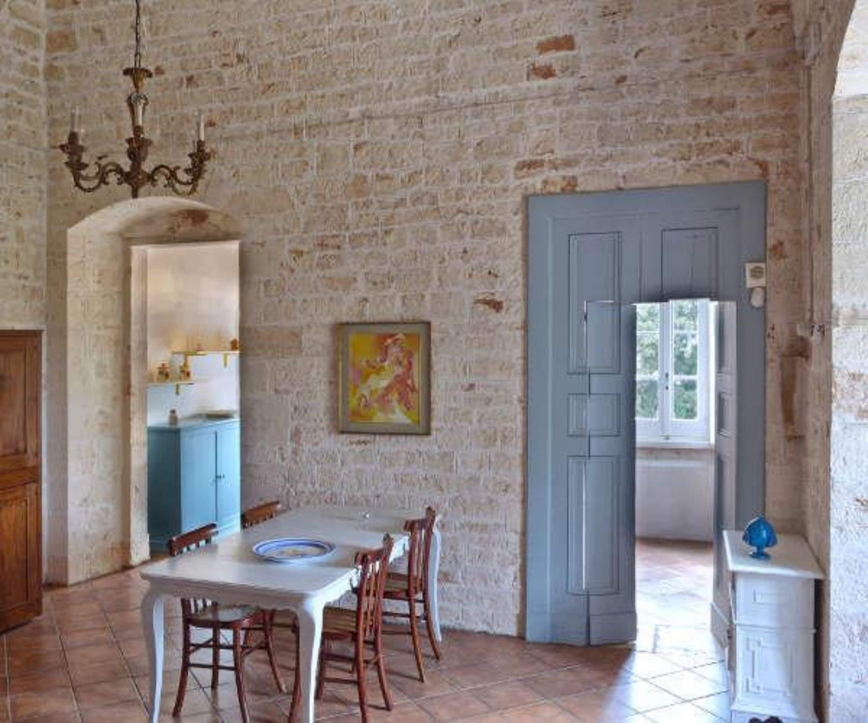 A rustic dining area with a brick wall, a blue door, and a painting on the wall.