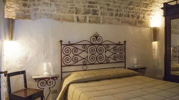 Un dormitorio con pared de piedra, estructura de cama de metal, mesita de noche con lámpara y una silla.