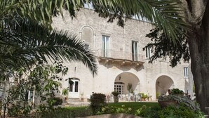 A stone building with arched windows and a courtyard with plants and a palm tree. - Agriturismo Antonelli Piangevino (Monopoli)