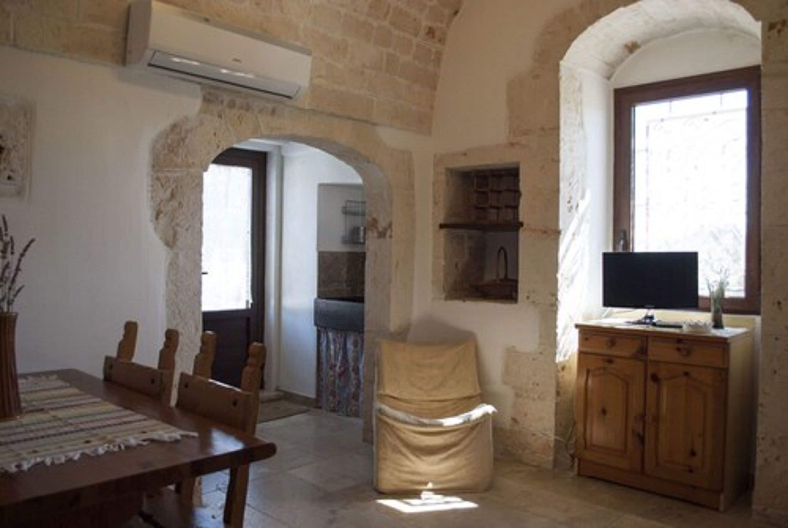A room with a wooden dining table, a covered chair, a wooden cabinet, and a television.