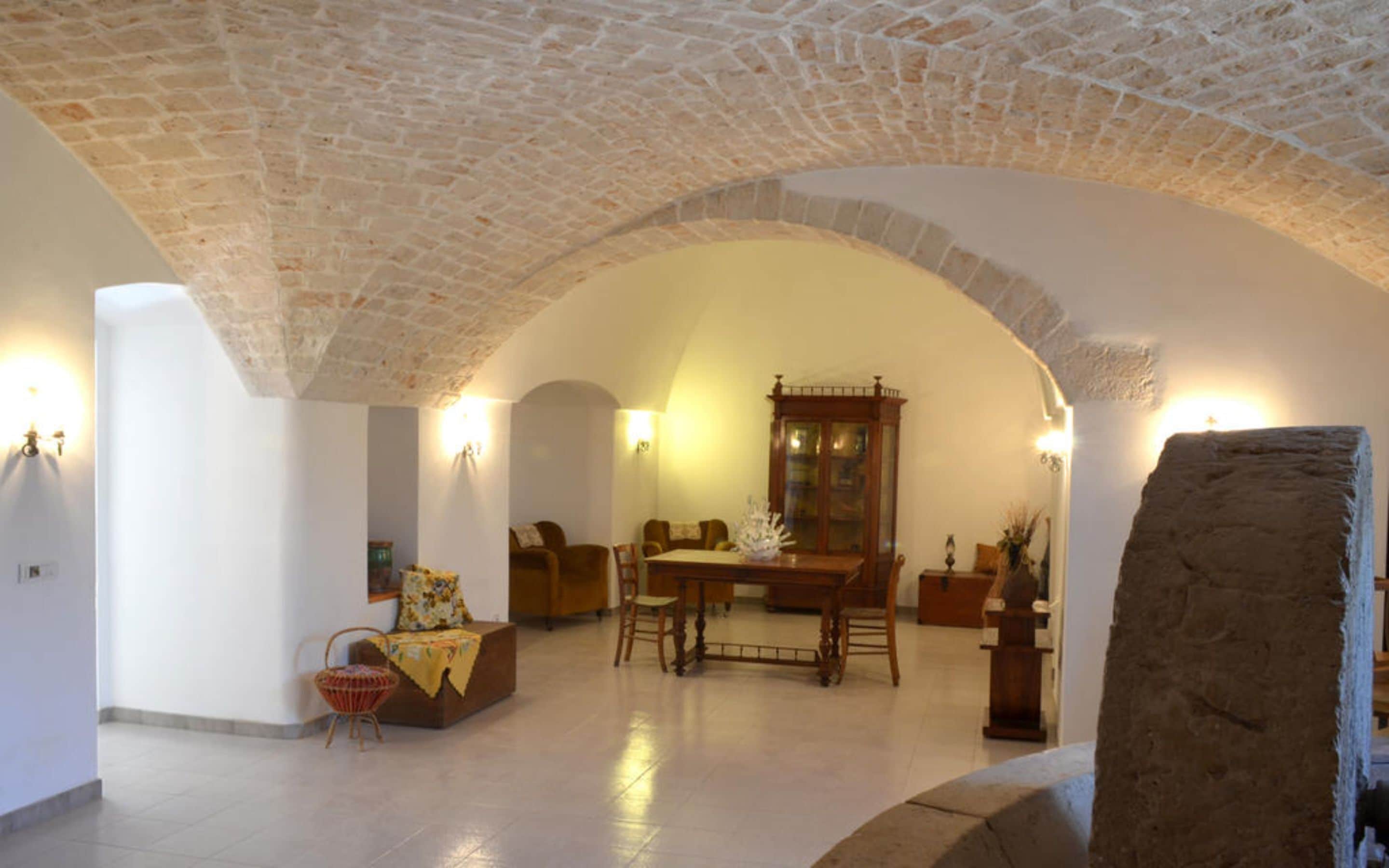 A spacious room with a high arched ceiling, a dining table with chairs, a fireplace, and a large stone block in the foreground.