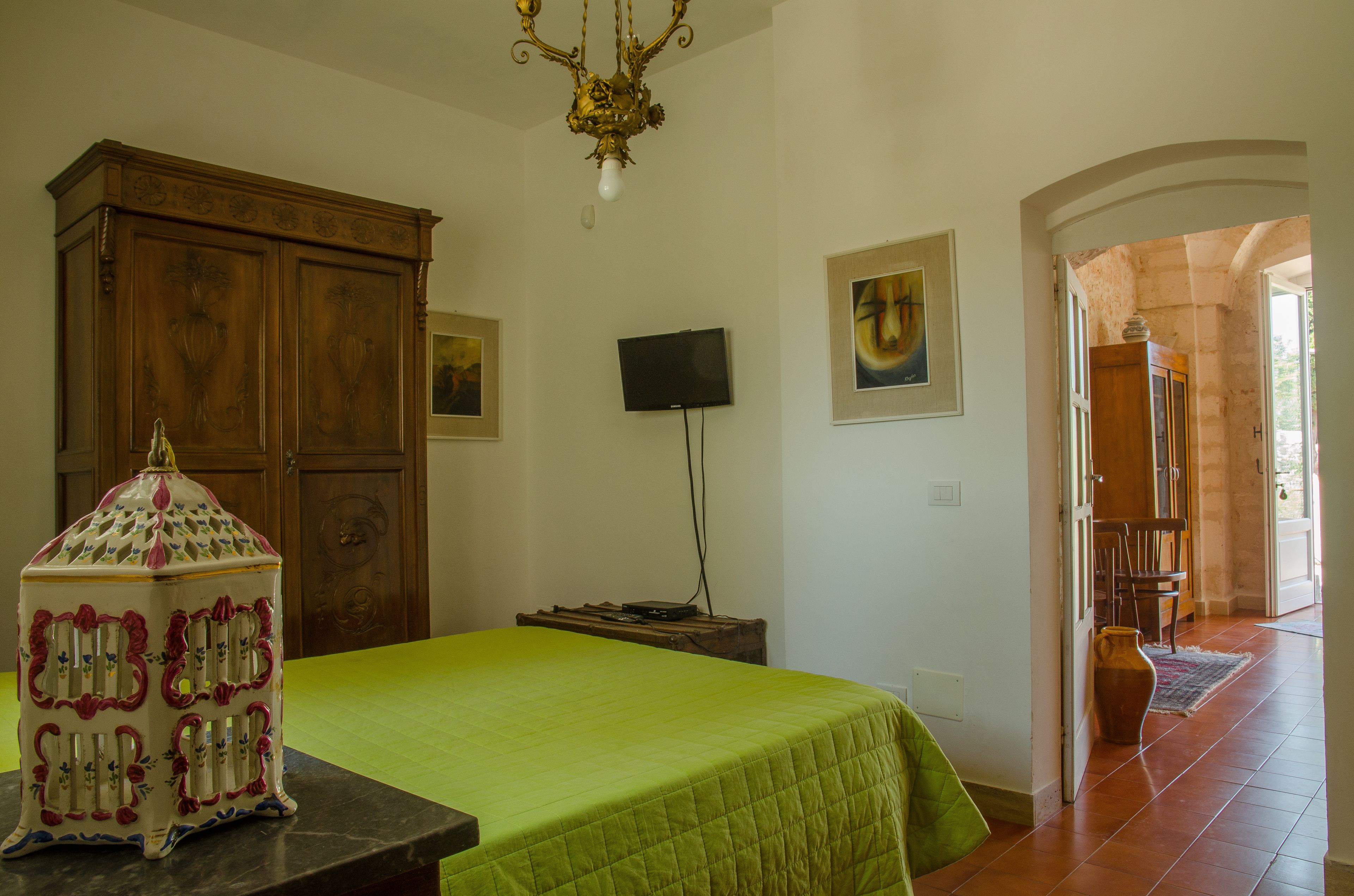 Un dormitorio con una colcha verde, un mueble de madera, un televisor y una pieza decorativa de cerámica.