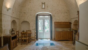 A stone-walled room with a wooden dining table and chairs, a small window, and a door leading outside. - Agriturismo Antonelli Piangevino (Monopoli)