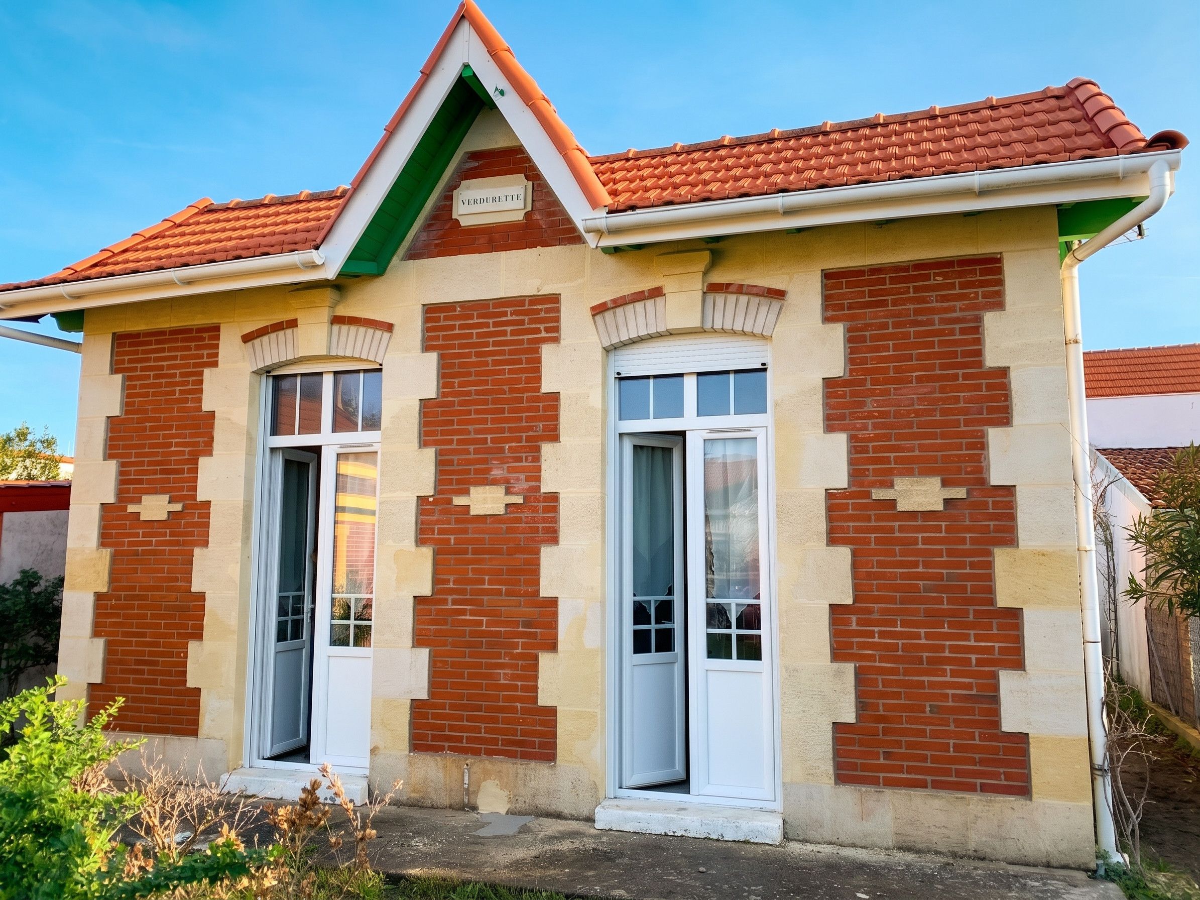 A two-story building with a red-tiled roof, brick facade, and white-framed windows.