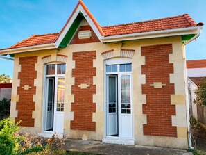 A two-story building with a red-tiled roof, brick facade, and white-framed windows. - Homerez - Charming House Soulac-sur-Mer, Garden, 65 m² (Soulac-sur-Mer)