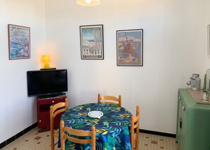 A small room with a TV, a table with chairs, and three framed pictures on the wall. - Homerez - Charming House Soulac-sur-Mer, Garden, 65 m² (Soulac-sur-Mer)