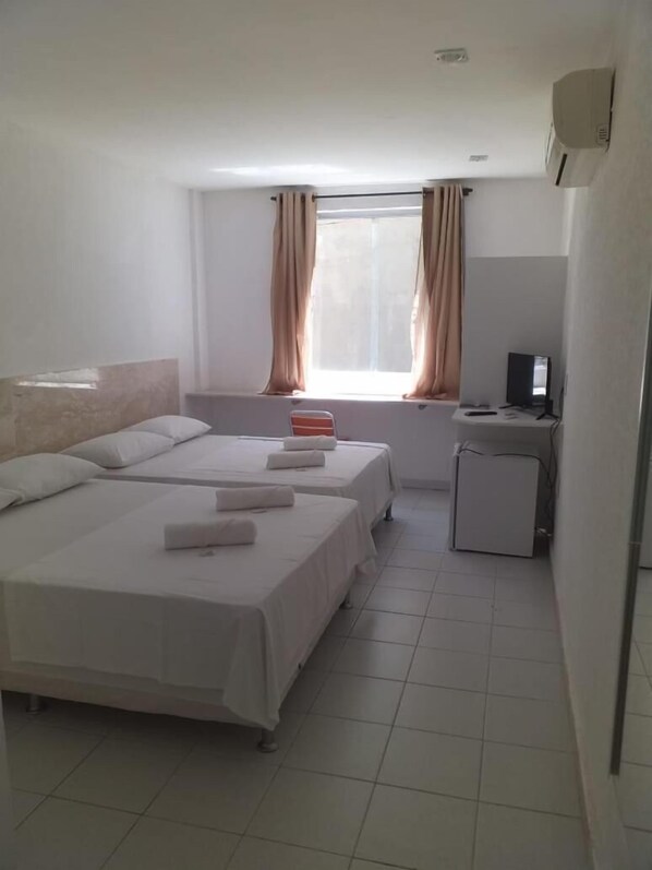 A hotel room with two beds, a small desk with a computer, and a window with curtains.