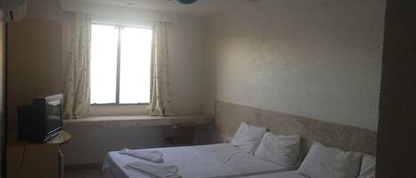 Habitación de hotel con dos camas, un televisor sobre un mueble, un ventilador de techo y una ventana con cortinas.