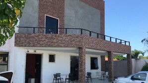 A two-story building with a balcony, a covered patio with chairs, and a car parked in the driveway. - Pousada Praia de Guarajuba (Camaçari)