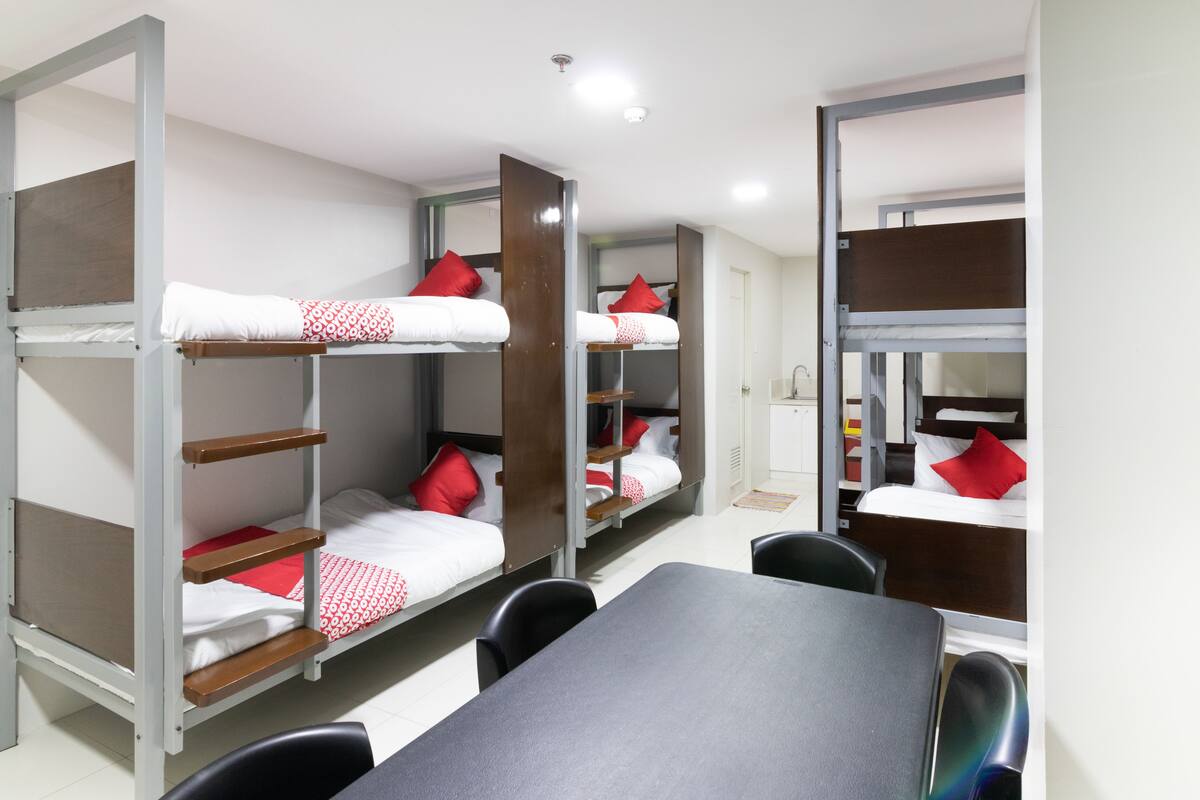 A dormitory room with bunk beds, a table, and chairs.