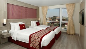 A hotel room with two beds, a large window with curtains, a TV, and a city view.