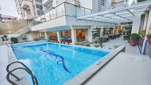 A swimming pool with a glass balustrade, surrounded by potted plants and outdoor seating.