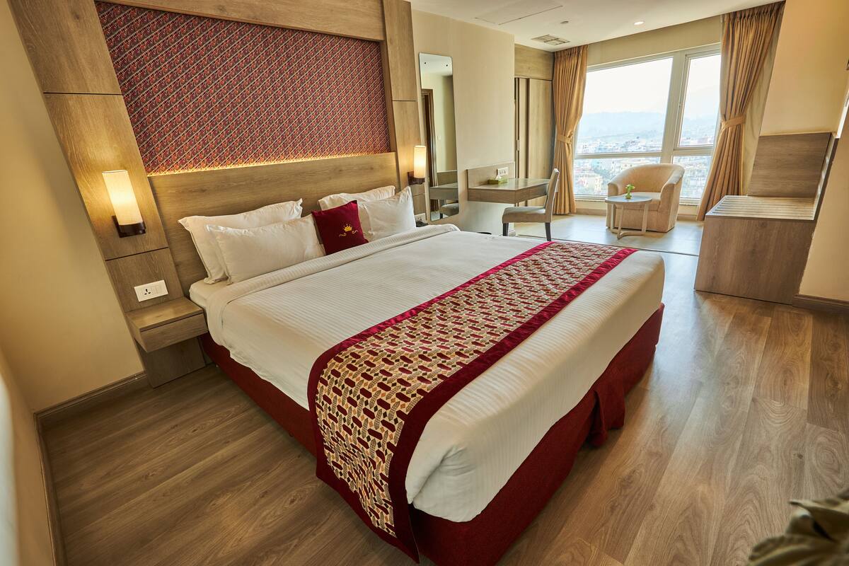 A hotel room with a large bed, a desk, a chair, and a view of the city.