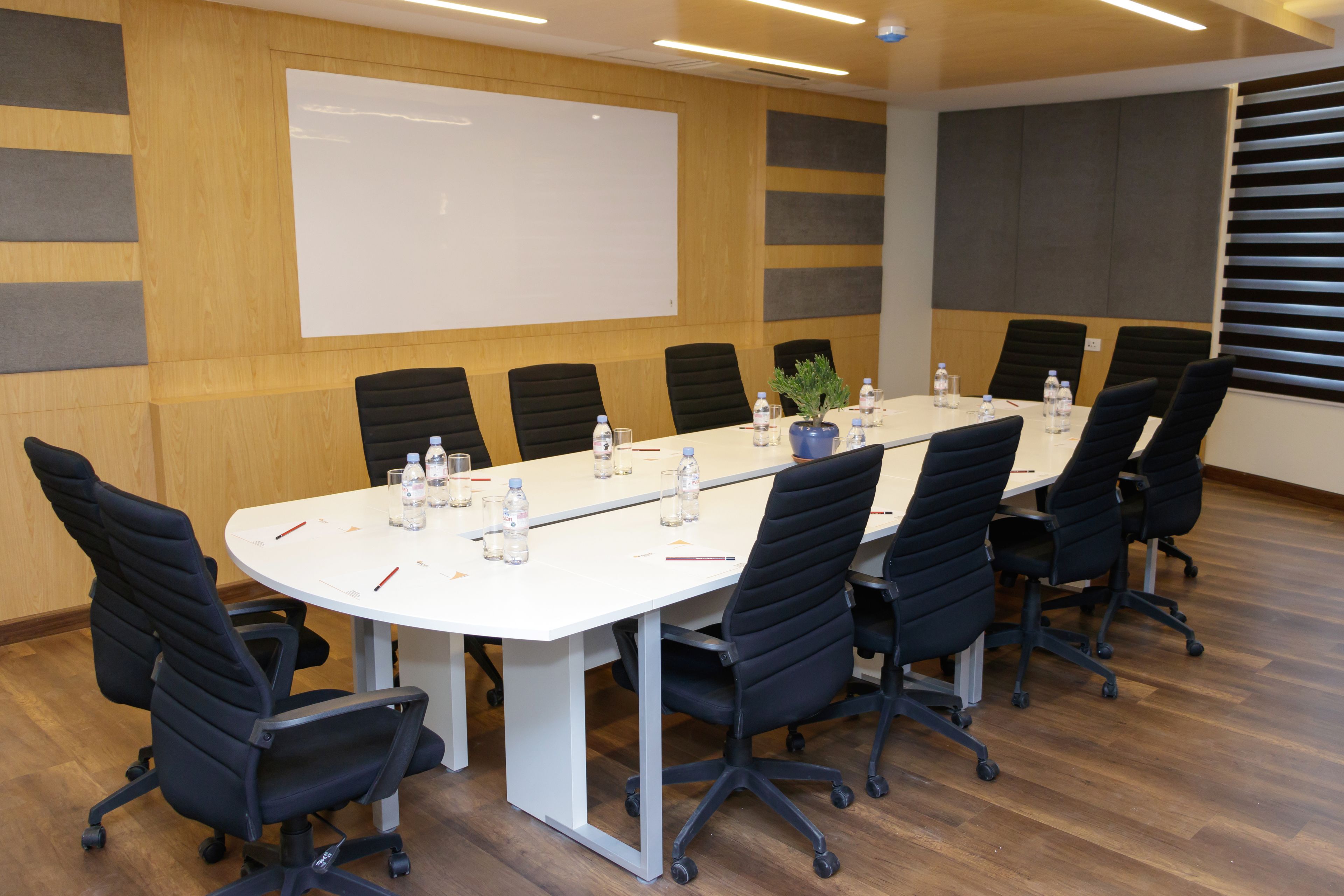 A conference room with a long table, black chairs, water bottles, and a whiteboard.