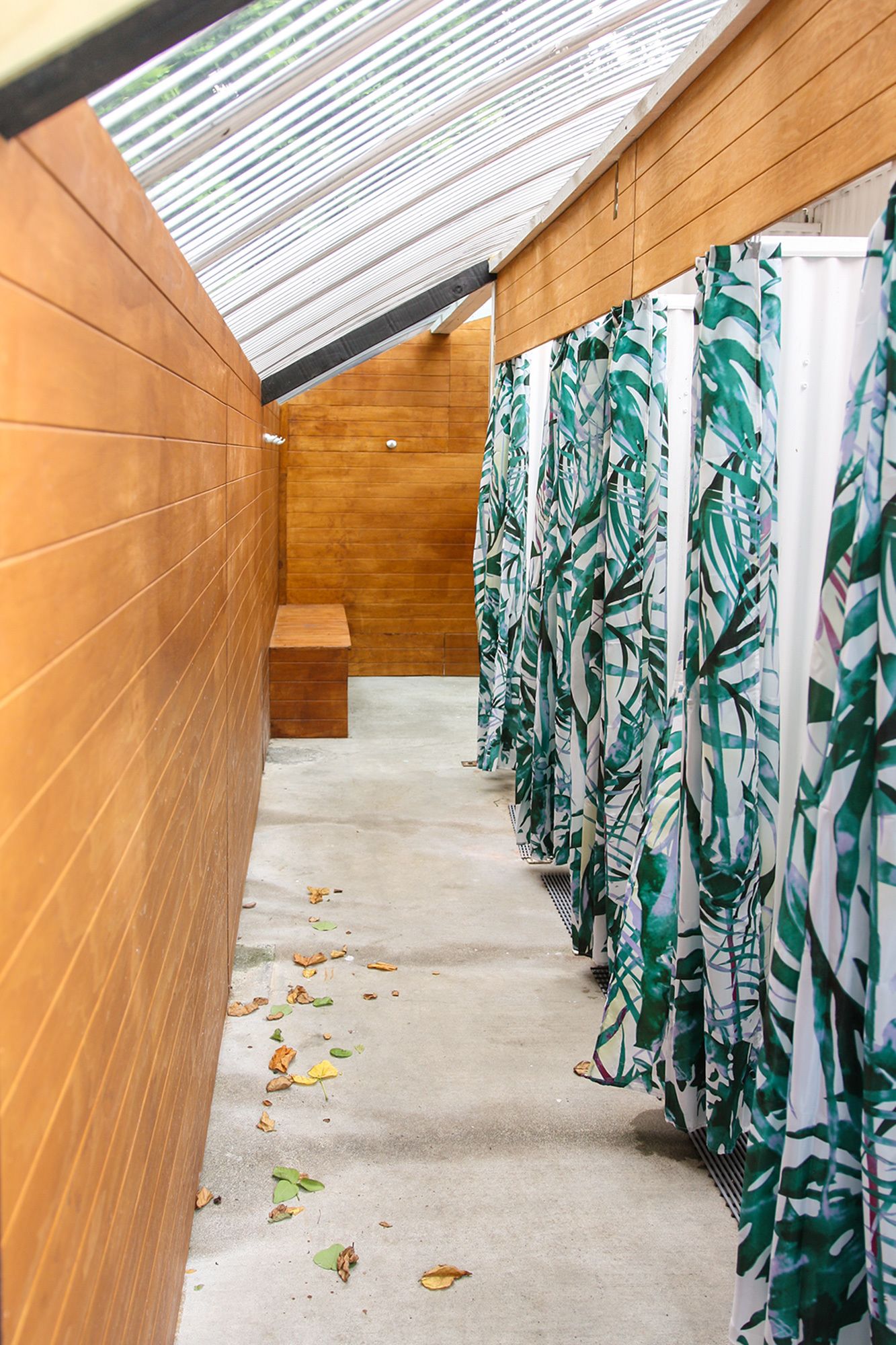 A corridor with wooden walls, a bench, and a row of shower curtains with a leaf pattern.