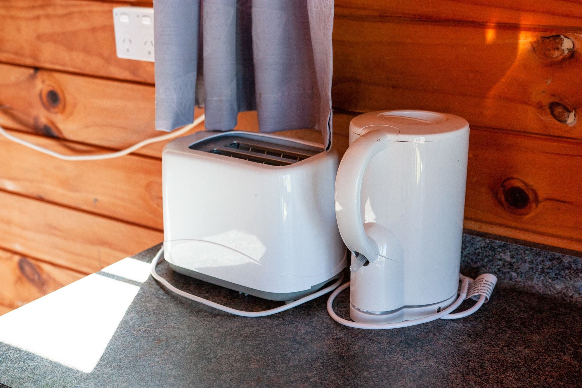A toaster and a coffee maker on a granite countertop with wooden paneling in the background.