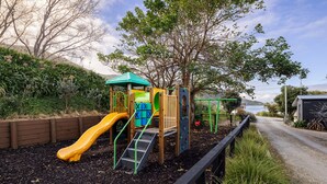 Un parque infantil con un tobogán amarillo, una estructura para escalar y una casita de juegos con techo verde.