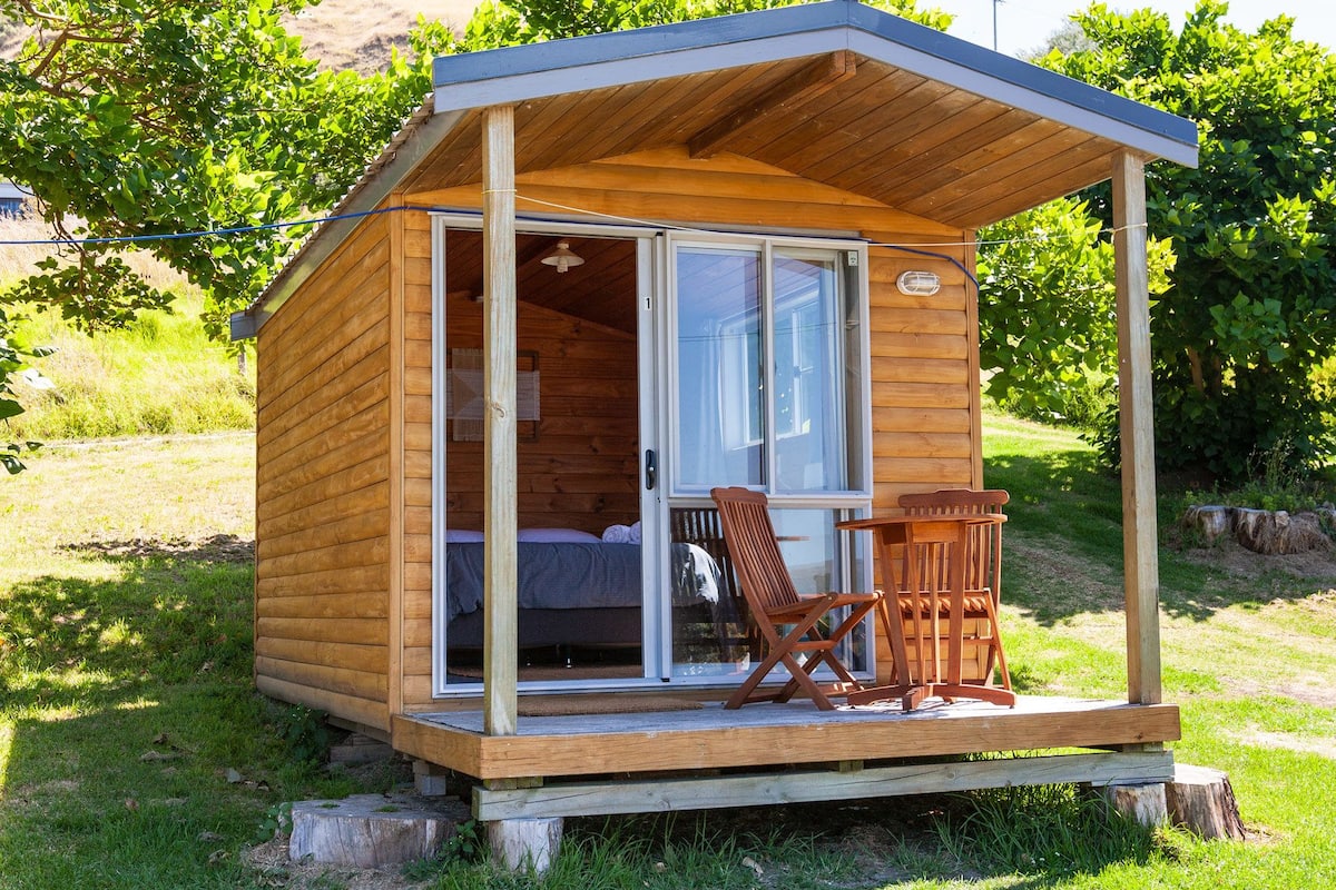 A wooden cabin with a porch, a bed, and a chair.