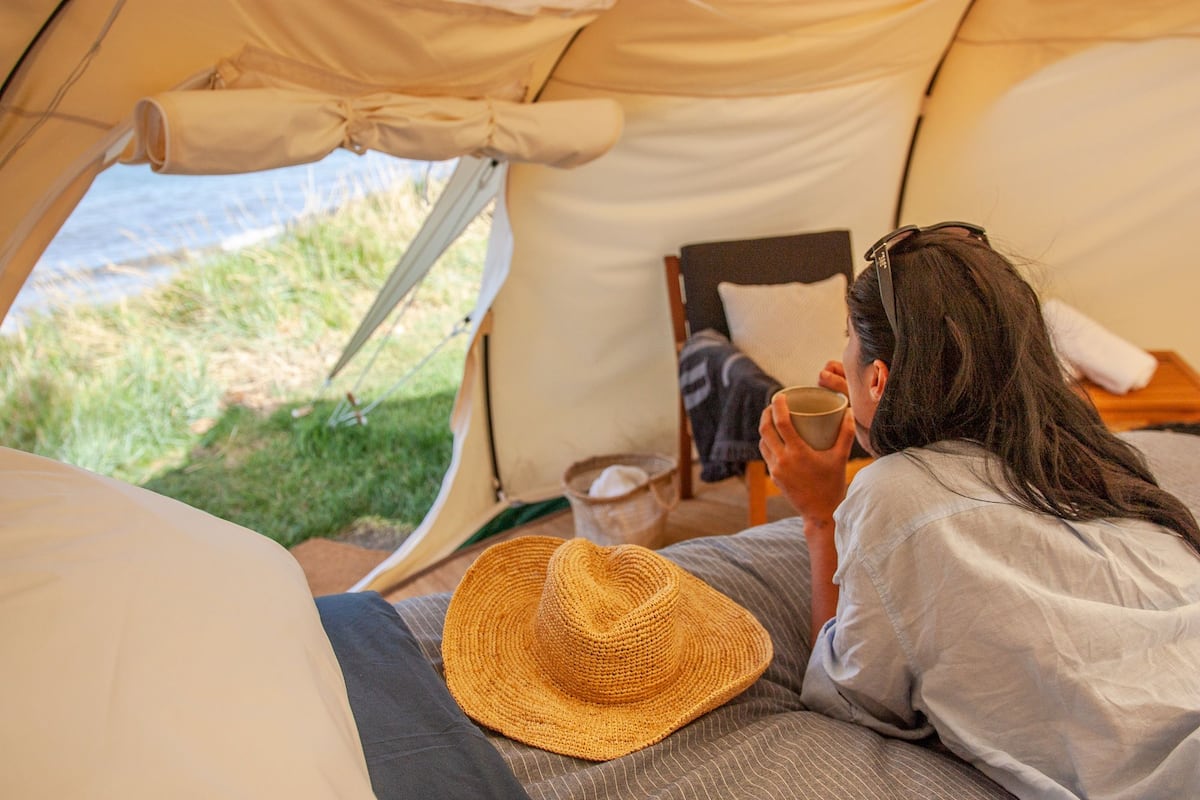A tent with a bed, a hat, and a person holding a cup.