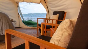 Una tienda de campaña con vistas al mar, muebles de madera y una mesa.